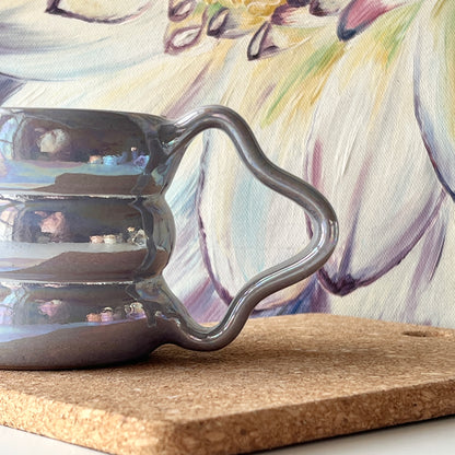 The handcrafted mug showcasing its shimmering luster and sculpted handle up close.