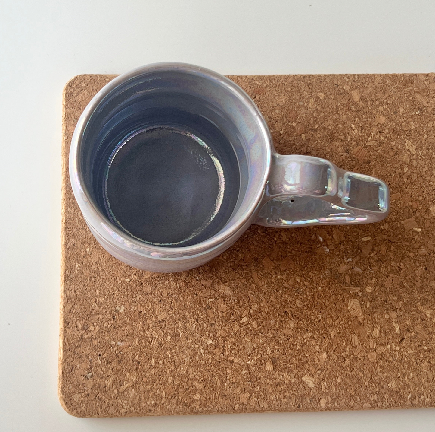 Top view of a handmade ceramic mug with a white iridescent glaze and wavy handle